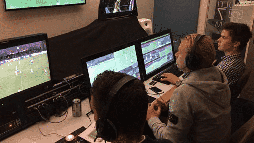 Three men sitting in front of screens displaying different shots of a football match.