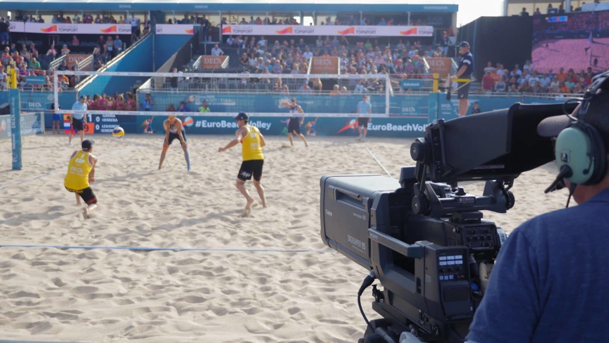 A camera operator filming a beach volleyball game.