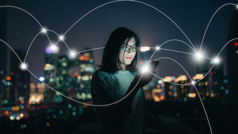 A woman using her phone with an illuminated city skyline in the distance. White lines show the digital connections being made across the city.