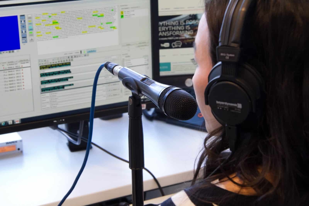 A subtitler sitting in front of a computer with a microphone in front of her.