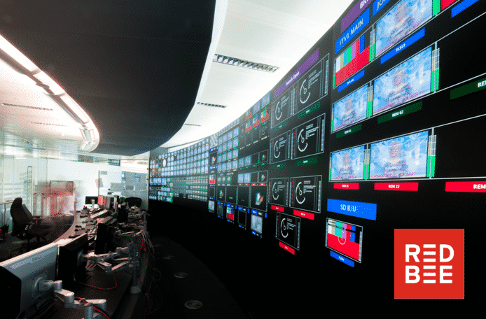 A long desk with computers in front of a wall of screens.