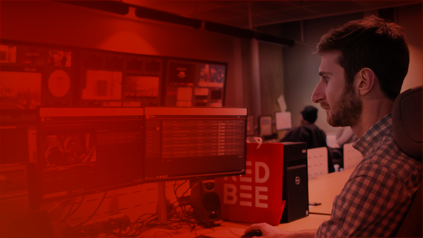 A red tinged image showing a man sitting in front of two computer screens.