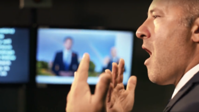 A close up of a man talking with his hands raised.