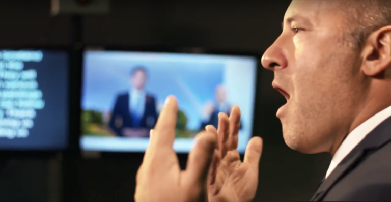 A close up of a man talking with his hands raised.