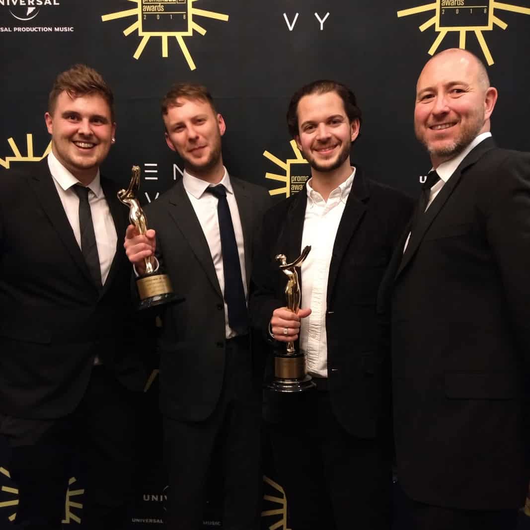 A group of four smartly-dressed men posing with two trophies.