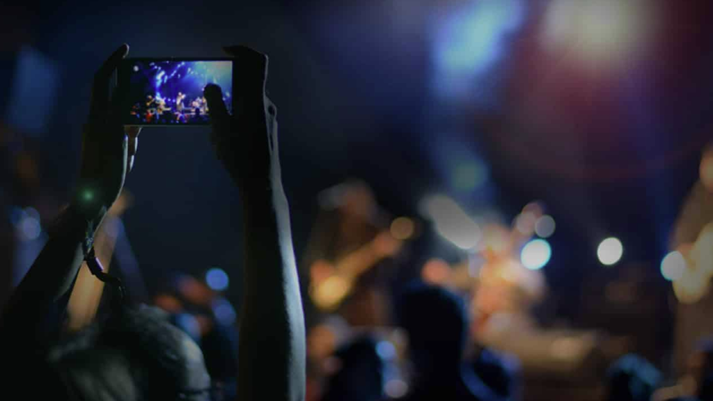 A person photographing the band at a gig on their phone.