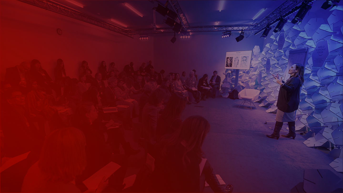 A red and blue tinged image showing a woman giving a presentation to people seated in rows.