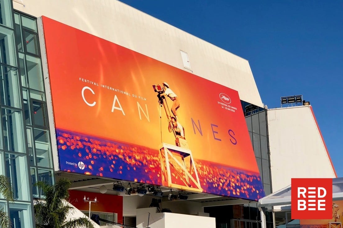 A large poster on a modern, glass-fronted building advertising the Cannes Film Festival.