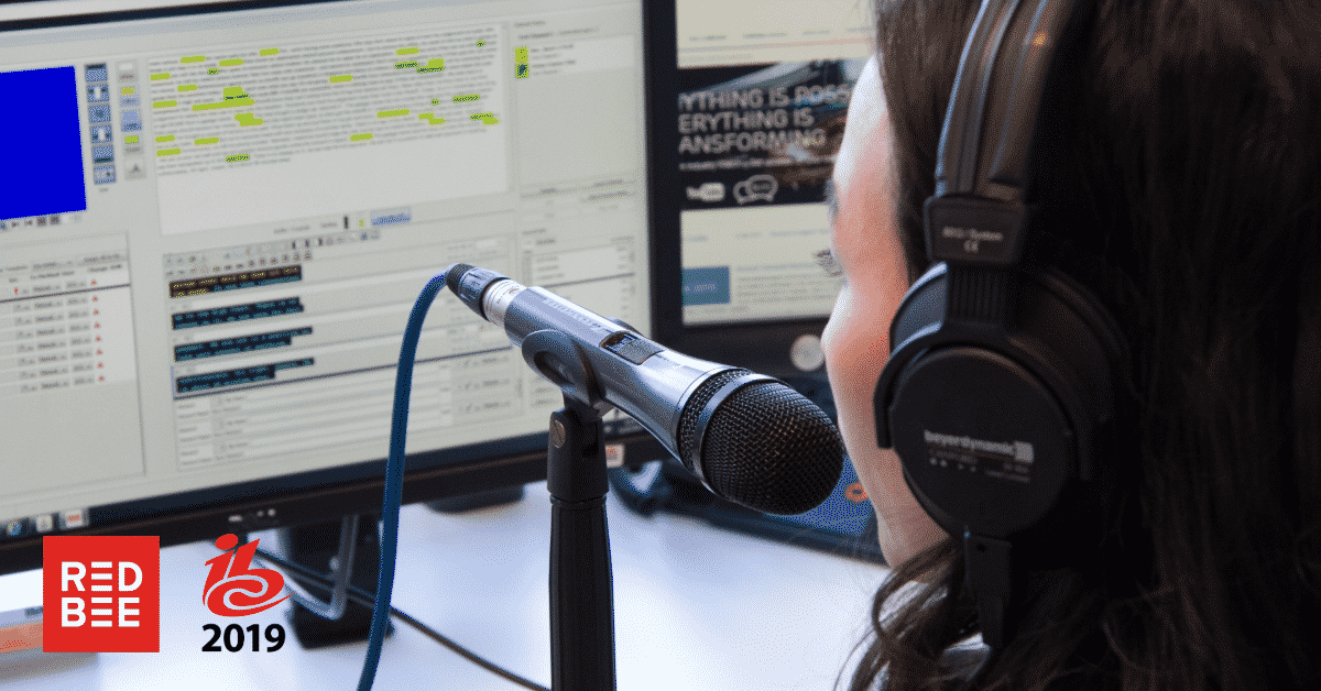 A subtitler sitting in front of a computer with a microphone in front of her.