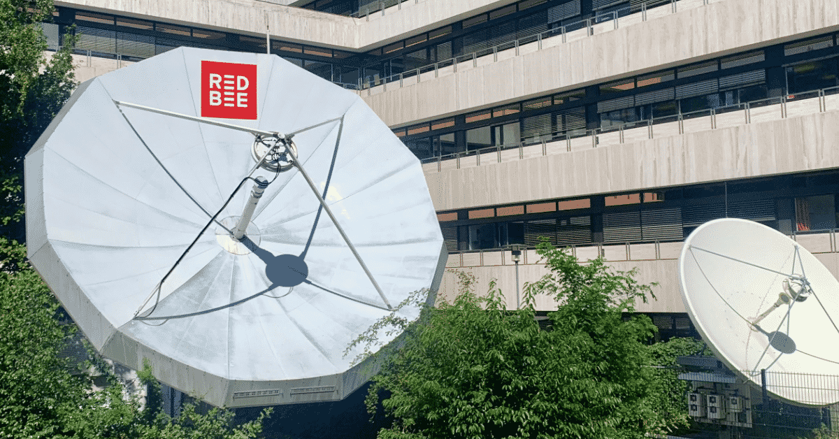 Two satellite dishes outside an office building. One of the dishes has the Red Bee logo on it.