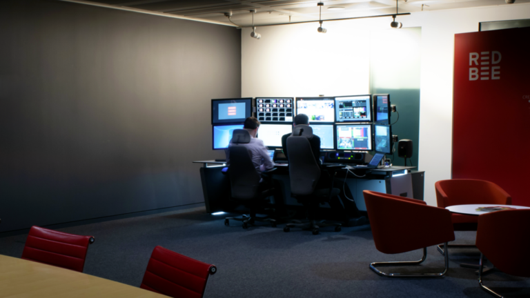 Two people sitting in front of several screens.