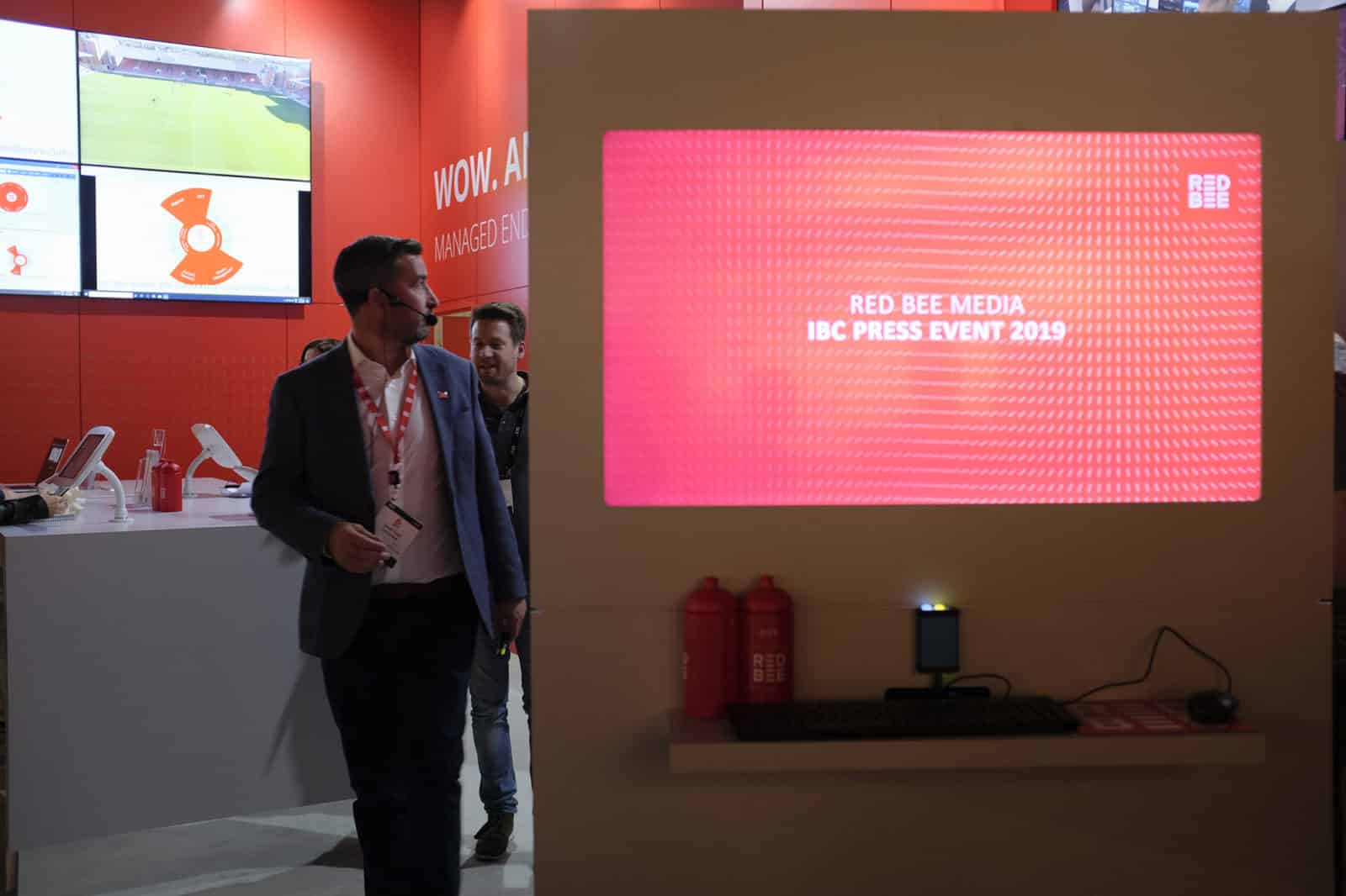 A man wearing a headset standing next to a wall with the words 'Red Bee Media. IBC Press Event 2019' projected onto it.