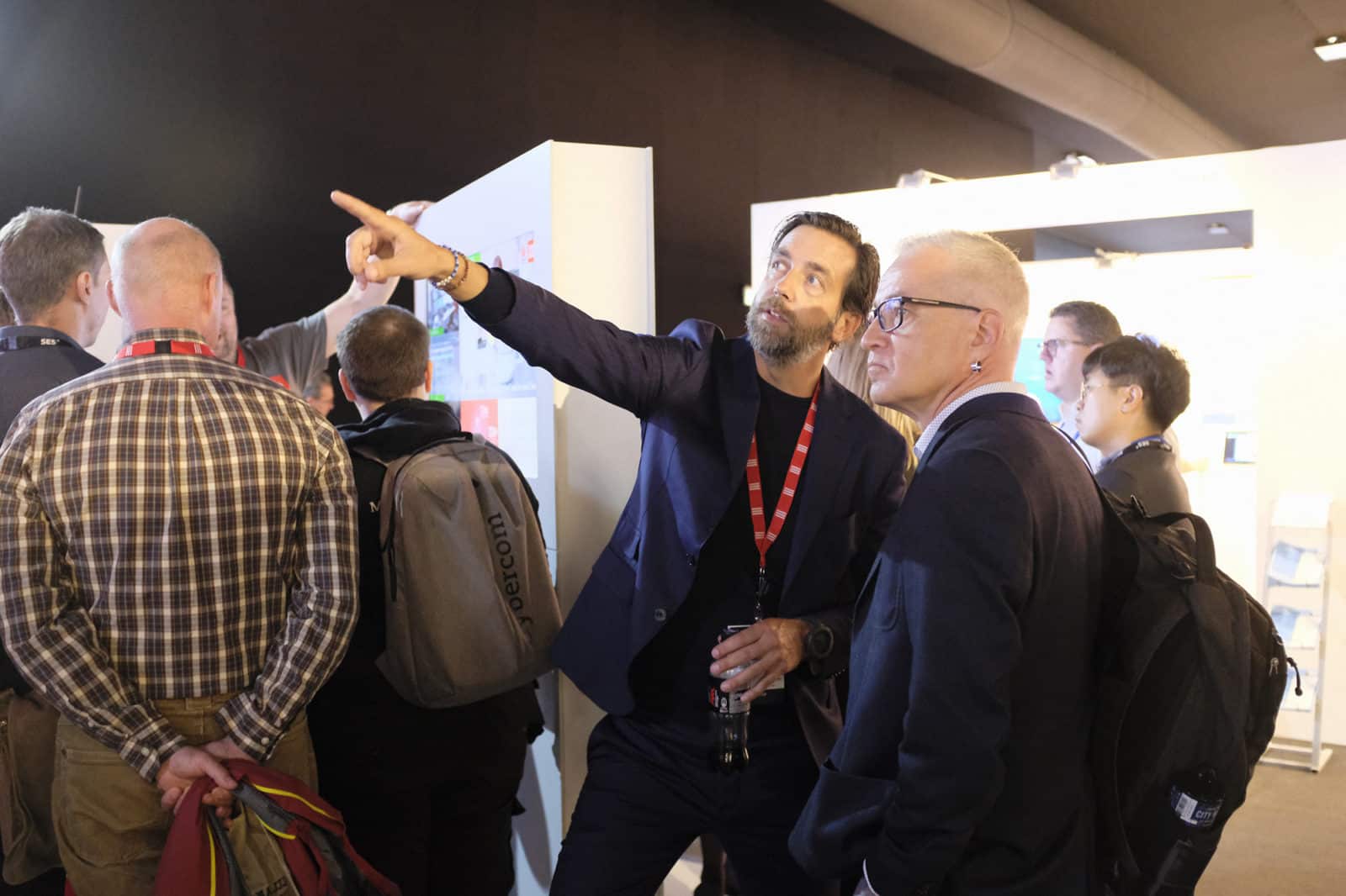 A man at a convention pointing something out to another man.