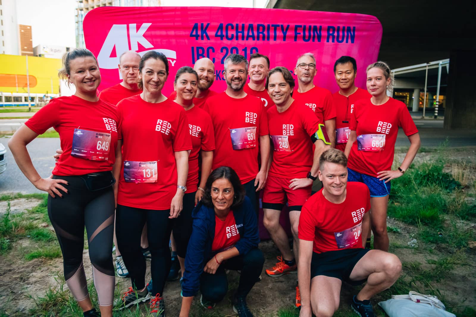 Red Bee employees in running gear posing in front of a '4K For Charity Fun Run' sign.