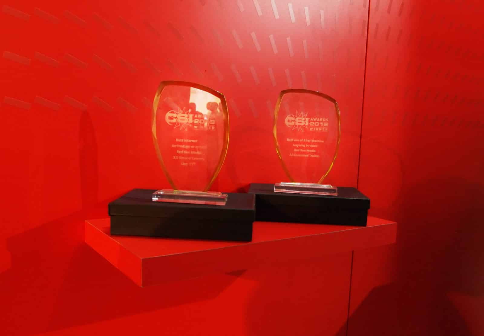 Two glass trophies sitting on a ledge on a red wall.