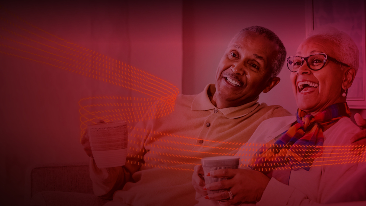 Red, dotted ribbons of light passing in front of a smiling man and woman sitting with mugs in their hands.