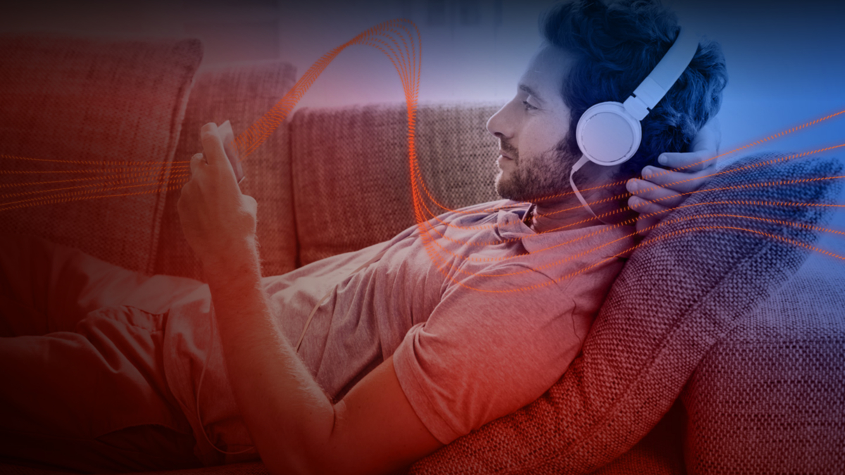 Red, dotted ribbons of light passing over a man wearing headphones and watching something on his smartphone.