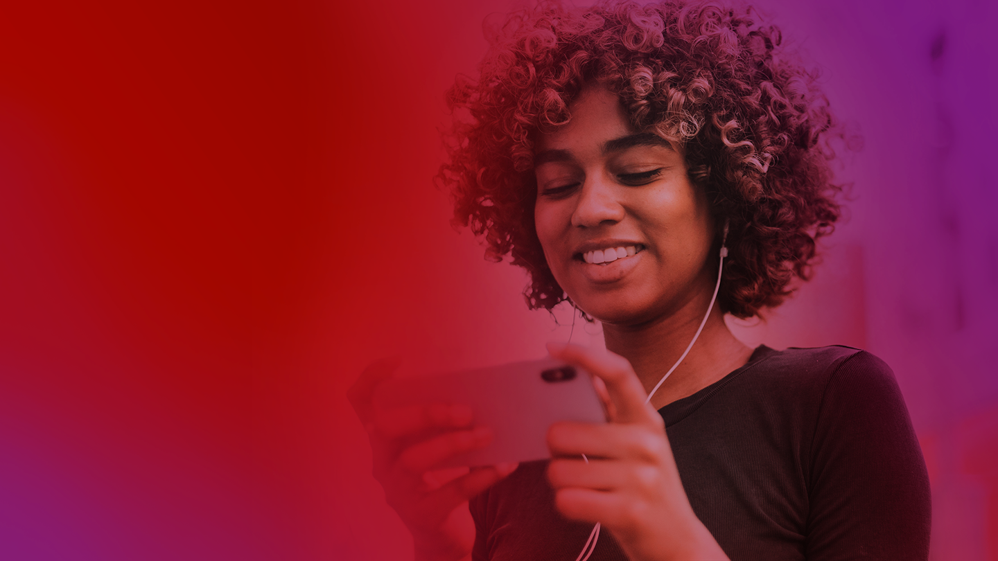 A red and purple tinged image showing a smiling woman wearing earphones and watching something on her smartphone.