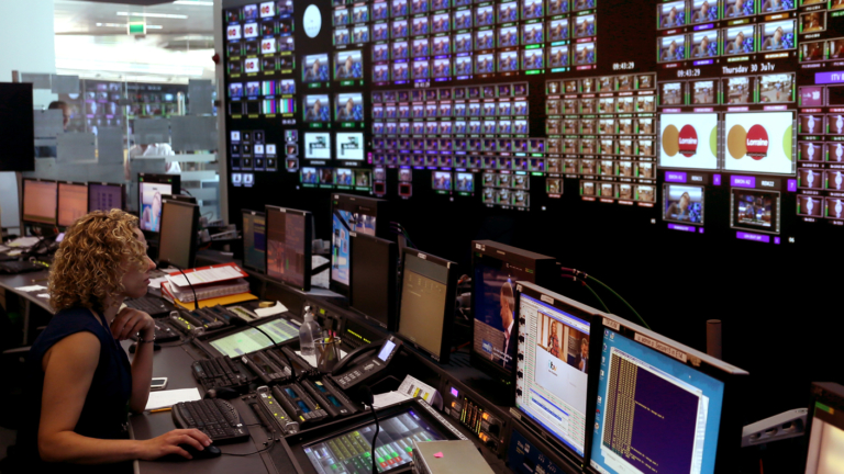 A woman facing a wall of screens in a playout suite.