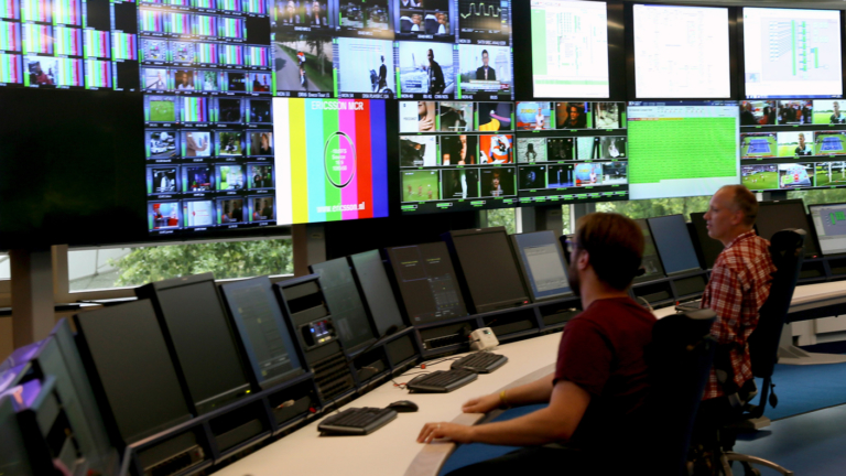 Two men sitting in front of dozens of screens in a playout suite.