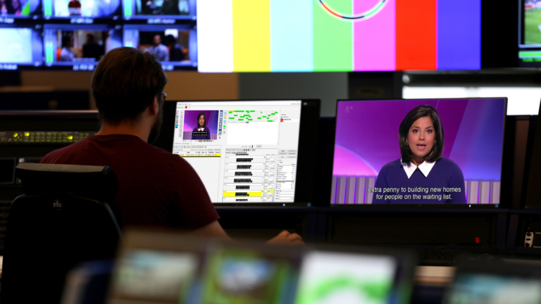 Man sitting in a Playout suite with pre-recorded subtitles on a screen.