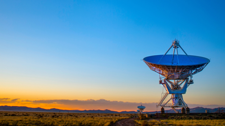 A row of large satellite dishes in a vast open plain, all pointing upwards.