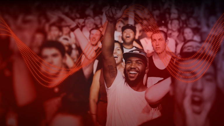 Man in a crowd, smiling and raising an arm.