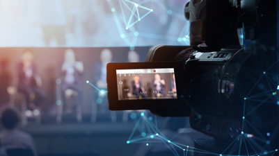 A camera recording speakers on a stage.