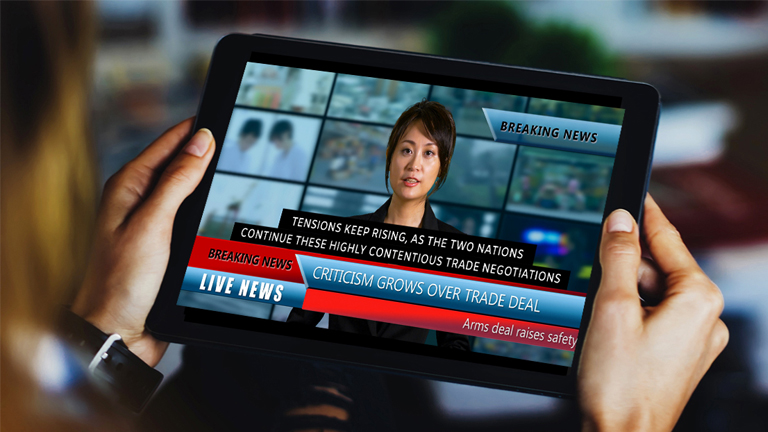 A breaking news story on a tablet screen. The headline reads, criticism grows over trade deal.