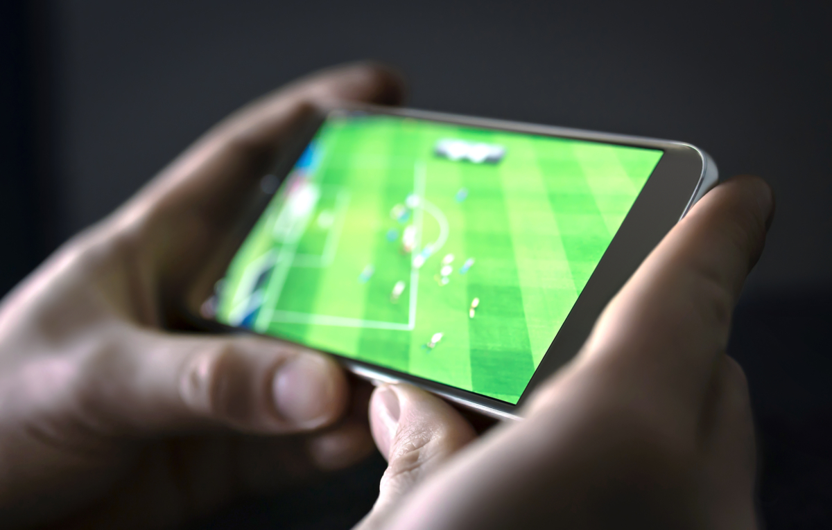 Hands holding a phone, showing a football match.