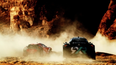 Two racing cars surrounded by a cloud of dust in a rocky, sunbaked landscape.