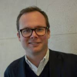 Tom Wootton, Head of Access & Solutions A smiling, clean-shaven man with short, brown hair and glasses.