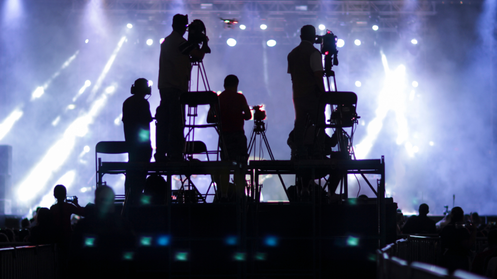 A camera crew silhouetted against white lights at an event.