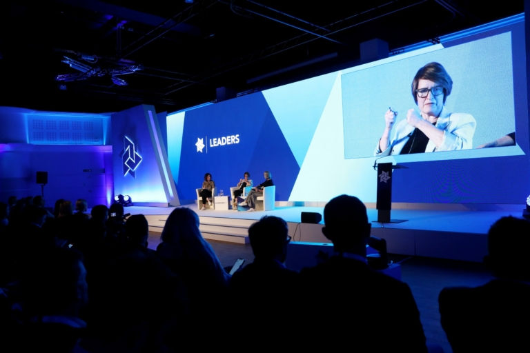 Three women sitting on a stage in front of a silhouetted audience.