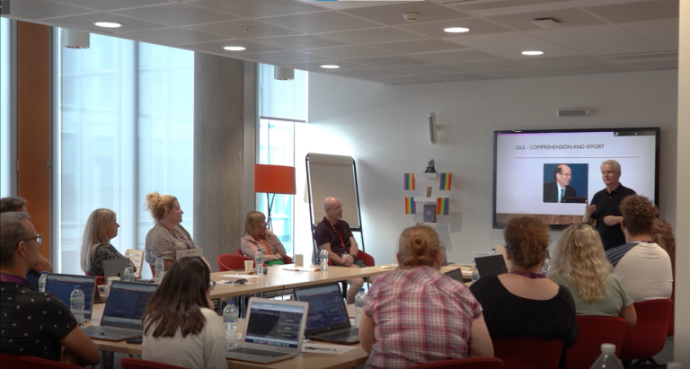 A man using sign language while addressing a group of people in a meeting room.