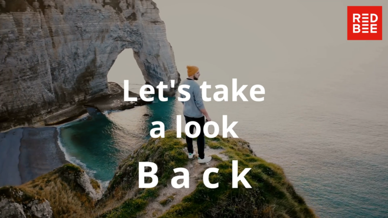 The Red Bee logo and the words 'Let's take a look back' over a photo of a man standing on a rock and looking out at the sea.