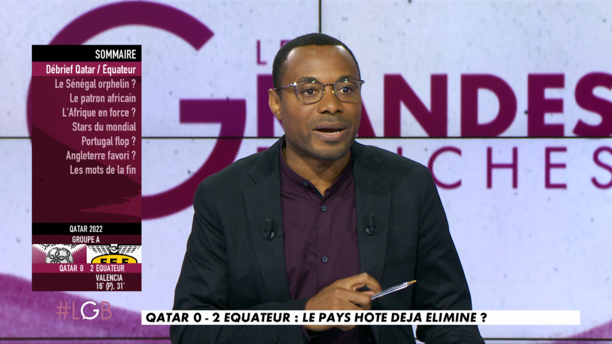 A screenshot from the French sports programme Les Grandes Bouches showing a man in front of a large screen in a studio.