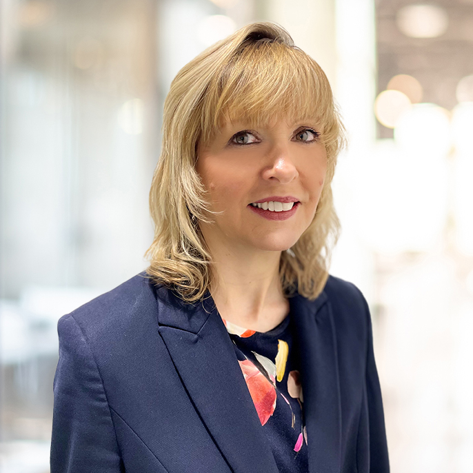 A smartly-dressed, smiling woman with shoulder-length, blonde hair and a full fringe.