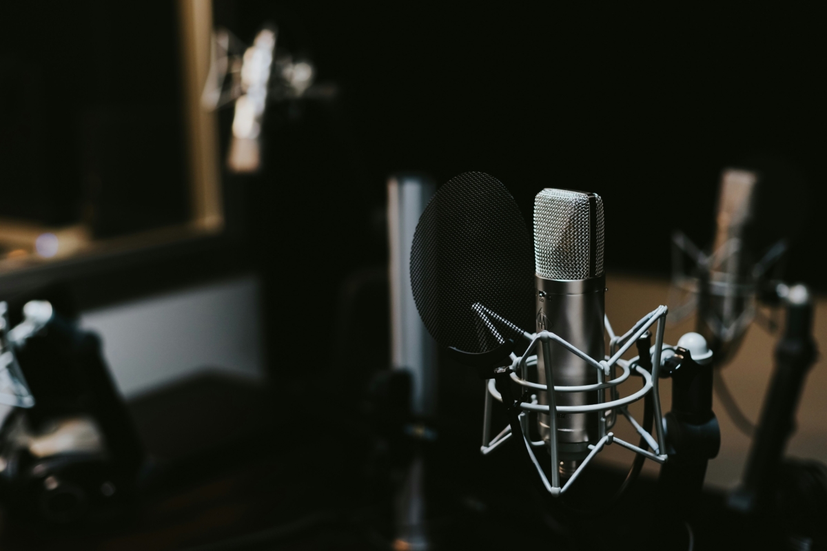 Close-up photo of a professional studio microphone with a pop filter in a dimly lit recording booth.